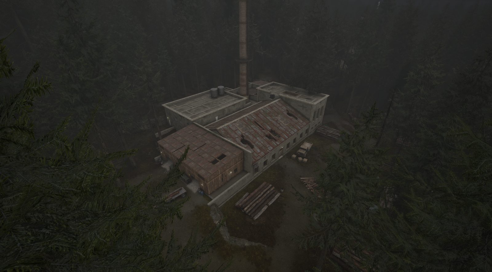 An aerial view of a long industrial building with a tall chimney, surrounded by dark forest