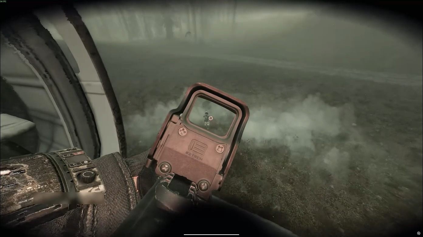 Inside a helicopter cabin, looking over a rifle's red dot sight at fog outside the window