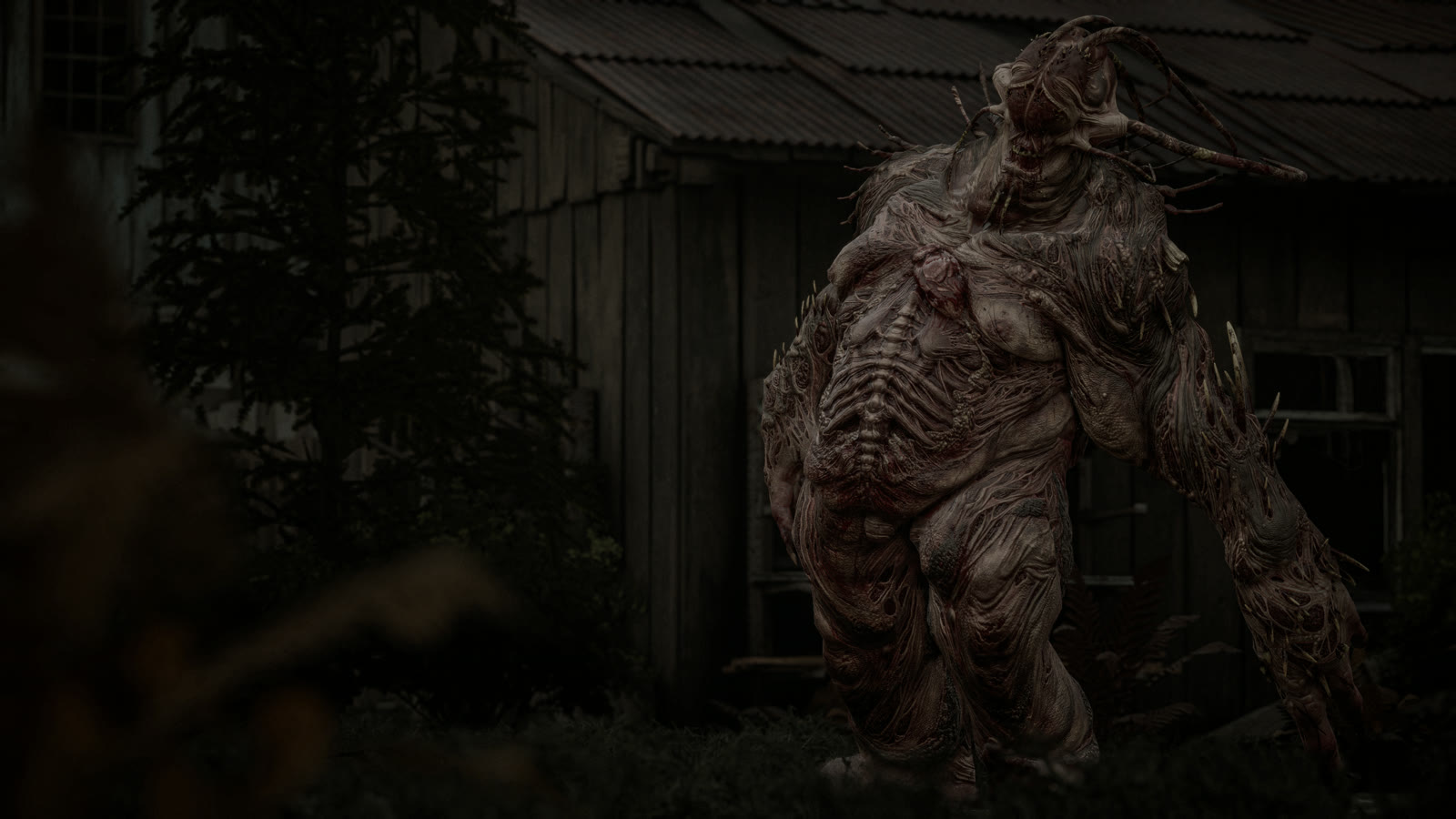 A hulking fleshy creature with a swollen ribbed body standing beside a dark wooden shed