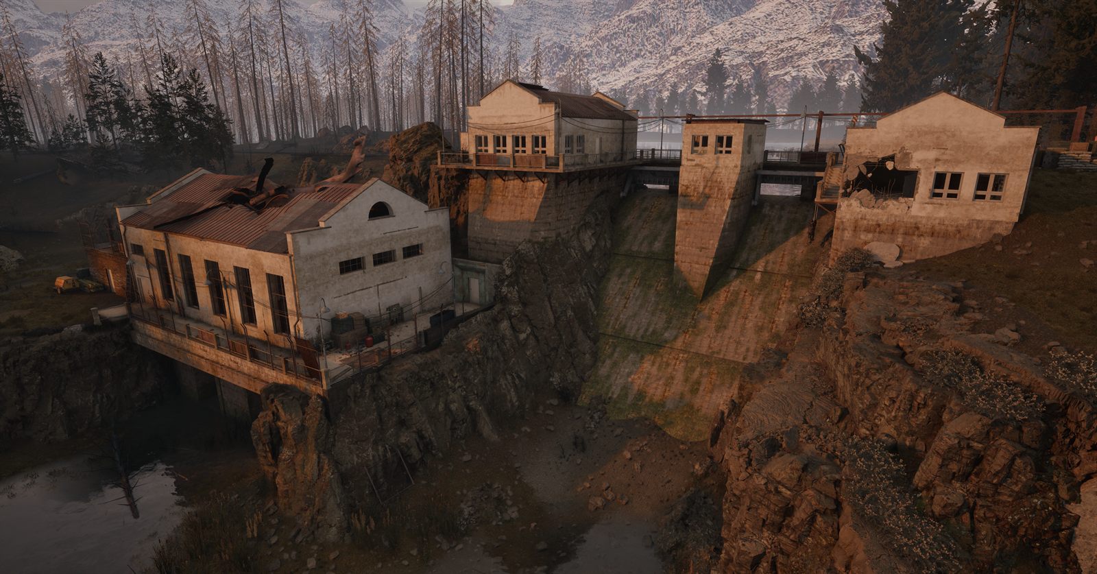 Concrete buildings on the edge of a deep flooded ravine, with pine forest and snowy peaks behind