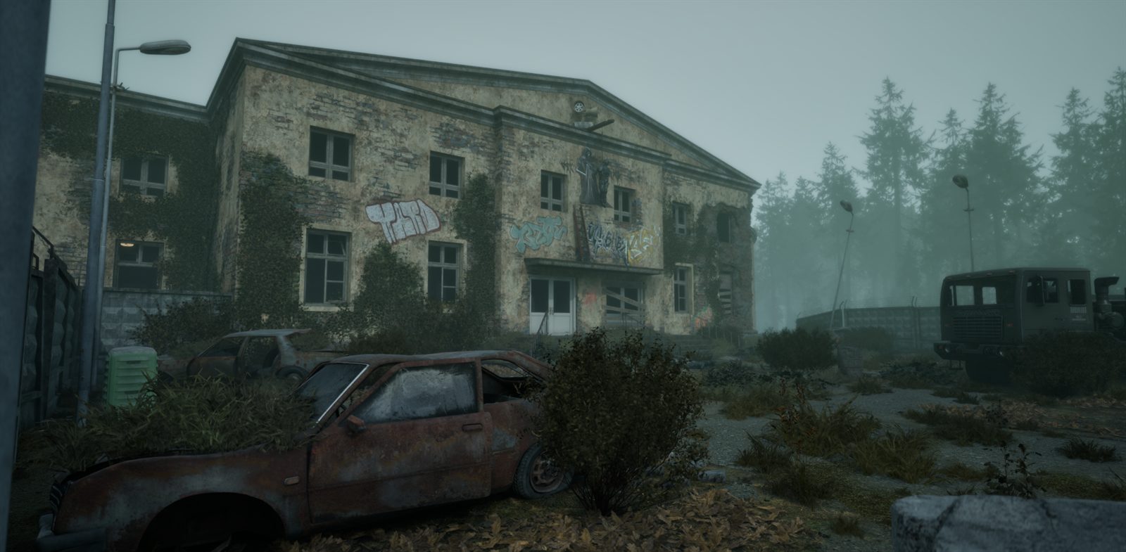 A derelict two storey building covered in graffiti and ivy, a rusted car and a military truck in front of it, pine forest in the fog